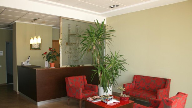 Zona de recepción con mostrador, dos sillas, una mesita de centro y una planta grande en maceta.