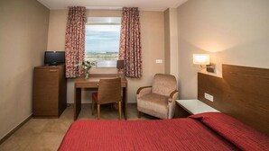 Habitación de hotel con cama, escritorio, silla, televisor y ventana con cortinas.