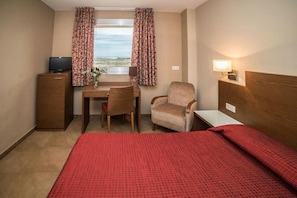 Habitación de hotel con cama, escritorio, silla, televisor y ventana con cortinas.