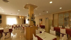 Un comedor de hotel con mesas dispuestas para el servicio, una zona de bar central y un amplio ventanal que proporciona luz natural.