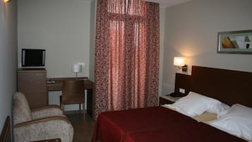 A hotel room with a bed, a desk, a chair, a television, and a painting on the wall.