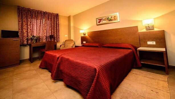 Una habitación de hotel con una cama grande, un escritorio, una silla, un televisor y un cuadro en la pared.