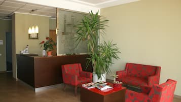 A reception area with a reception desk, two chairs, a coffee table, and a large potted plant.