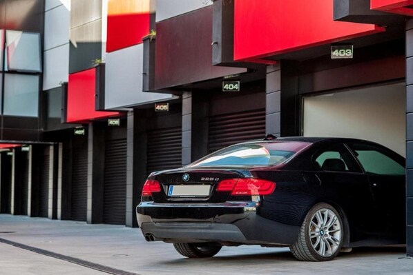 A black BMW 325d parked in front of a building with numbered garage doors.
