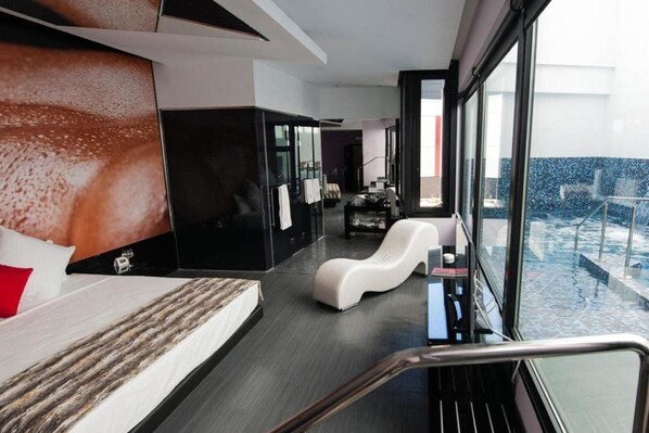A modern hotel room with a large bed, a seating area, and a view of a pool. - Hotel Loob Madrid (Torrejón de Ardoz)