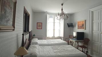 A hotel room with two beds, a chandelier, a television, and a window with natural light.