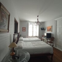 Habitación de hotel con dos camas, un candelabro, un televisor y una ventana con luz natural.