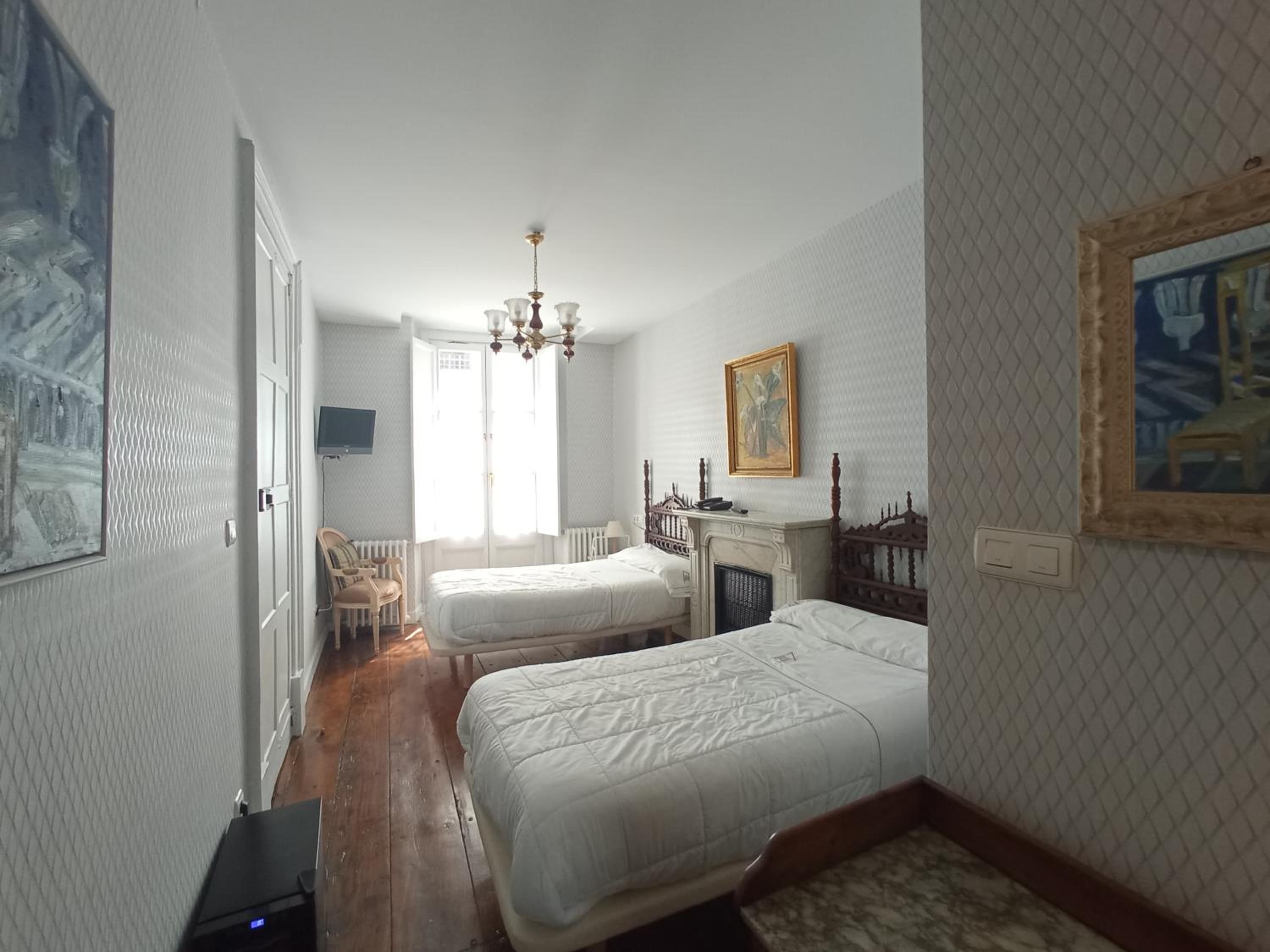 A bedroom with two beds, a chandelier, a fireplace, and a television.