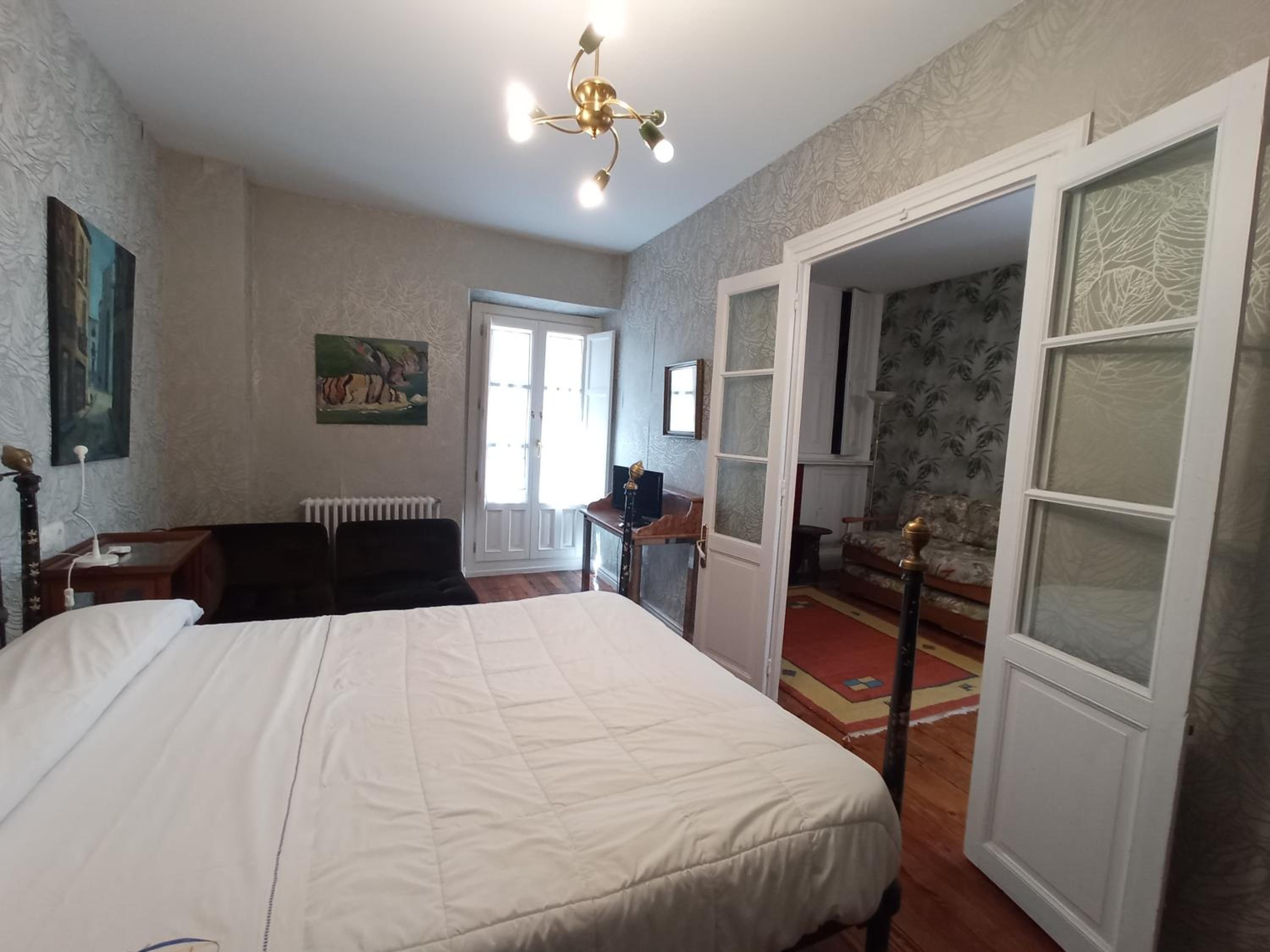 A bedroom with a large bed, a desk, a chair, a radiator, and a door leading to another room.