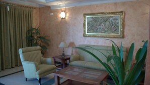 Una sala de estar con sofá, sillón, mesa de centro, lámpara y un cuadro grande en la pared.