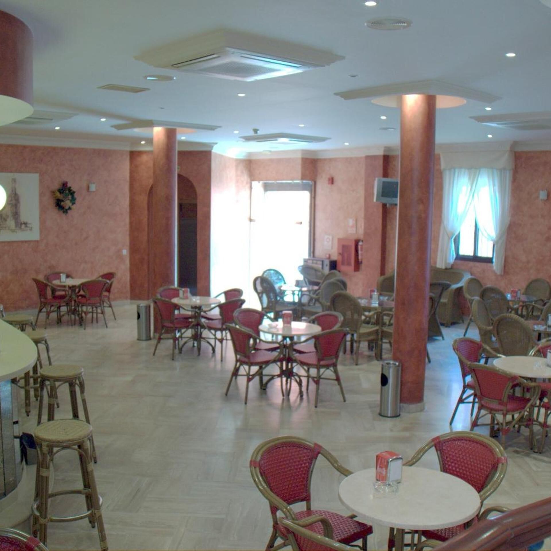 A spacious dining area with multiple round tables and wicker chairs, featuring a neutral color palette and a ceiling with recessed lighting.