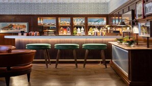 A bar area with wooden paneling, green bar stools, and a variety of bottles on shelves. - The White Hart Hotel Lincoln (Lincoln)