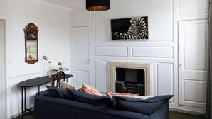 Un salon avec un canapé foncé, une cheminée, un miroir et un tableau représentant une zèbre accroché au mur.