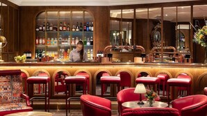 Un espace bar avec un barman, des fauteuils en cuir rouge et un comptoir où sont exposées différentes bouteilles.