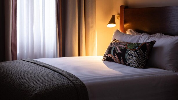 Une chambre d’hôtel avec un lit, une lampe de chevet et une fenêtre avec des rideaux.