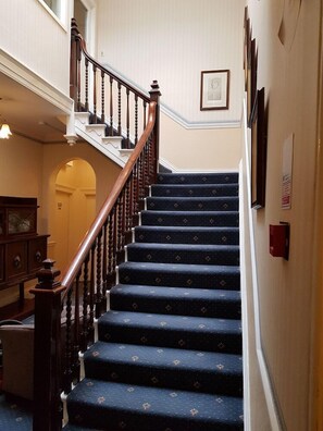 A staircase with dark carpeted steps and wooden railings. - The Hand Hotel (Llangollen)