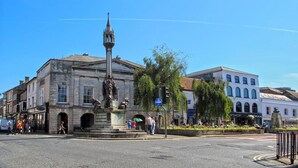 Ett torg med en central staty, omgivet av byggnader, och en klarblå himmel.