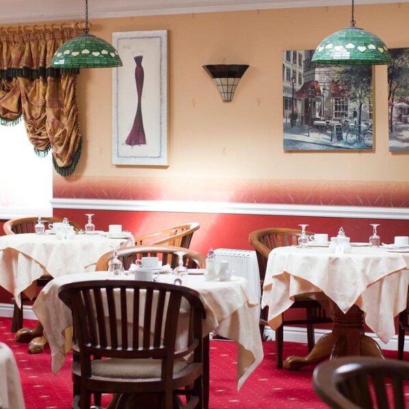 Un comedor con mesas dispuestas para el servicio, sillas y lámparas colgantes.