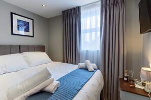 A hotel room with a bed, a bedside table with a lamp, and a window with curtains. - The Arc Hotel (Liverpool)