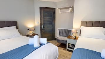 Quarto de hotel com duas camas, uma cadeira, uma mesinha de cabeceira e um aquecedor fixado na parede.
