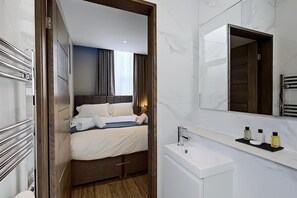 A hotel room with a bed, a bedside table, a mirror, and a bathroom with a sink and toiletries. - The Arc Hotel (Liverpool)
