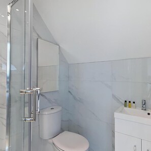 A modern bathroom with a glass shower enclosure, a toilet, and a vanity with toiletries. - The Arc Hotel (Liverpool)