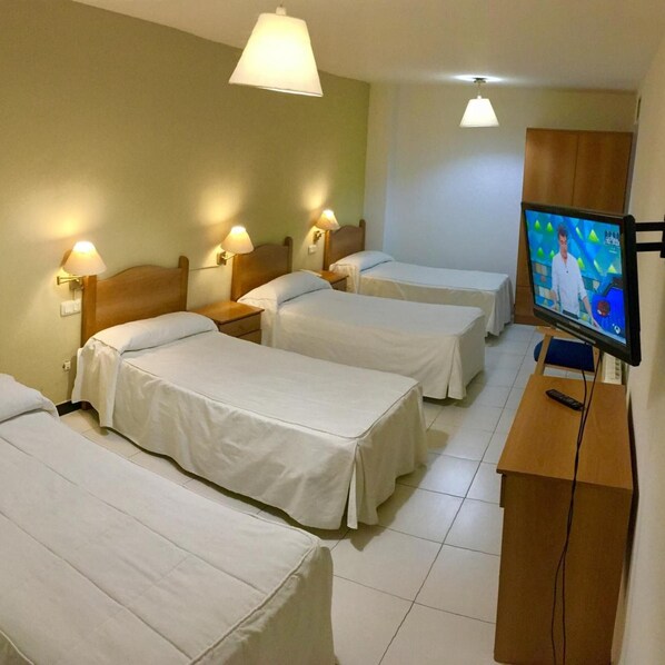A hotel room with four single beds, a television on a wooden stand, and wall-mounted lamps.