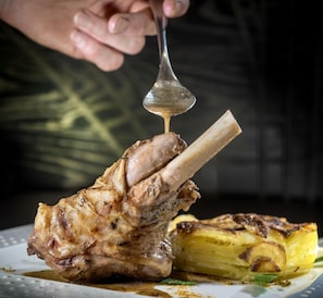 Un palillo de cordero con salsa y patatas asadas en un plato.