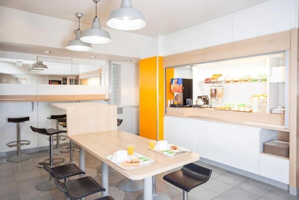 Een moderne keuken met een lange aanrecht, barkrukken en een feloranje accentmuur.