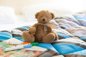 Ein Teddybär auf einem Bett mit gestreifter Bettwäsche und einer karierten Schleife.