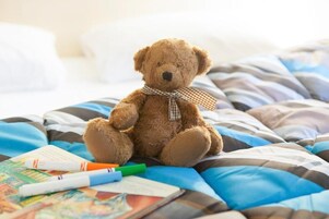 Un oso de peluche sobre una cama con ropa de cama a rayas y un lazo de cuadros.