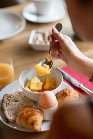 Una colazione con una ciotola di frutta, pane tostato e un croissant su un piatto.
