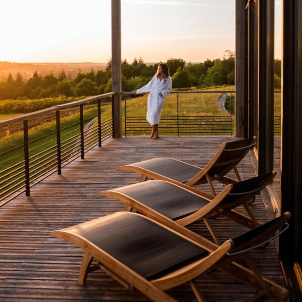 Une terrasse en bois avec des chaises longues et une personne vêtue d’une robe blanche.