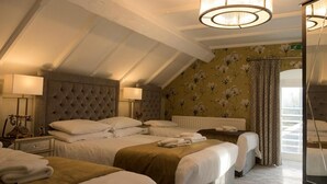 Une chambre d’hôtel dotée d’un plafond voûté, d’un grand lit avec une tête de lit capitonnée, de deux tables de chevet avec des lampes, et offrant une vue sur l’extérieur grâce à une fenêtre agrémentée de rideaux.