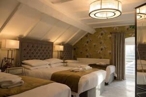 Habitación de hotel con techo abovedado, cama grande con cabecera capitonada, dos mesitas de noche con lámparas y vistas al exterior a través de una ventana con cortinas.