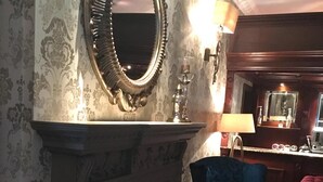 Une pièce avec une cheminée, un fauteuil bleu, un miroir et une lampe.