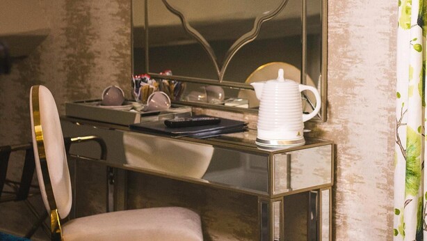 Une pièce comprenant une coiffeuse avec un miroir, un pichet blanc et un téléviseur fixé au mur.