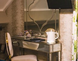 Una habitación con un tocador con espejo, una jarra blanca y un televisor montado en la pared.