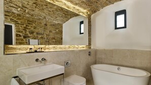 A bathroom with a stone wall, a large mirror, a sink, a toilet, and a bathtub. - The Bodmin Jail Hotel (Bodmin)