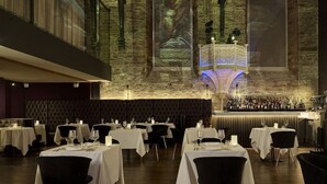 A restaurant with multiple tables, a bar area, and a large projection screen displaying a forest scene. - The Bodmin Jail Hotel (Bodmin)