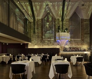 A restaurant with multiple tables, a bar area, and a large projection screen displaying a forest scene. - The Bodmin Jail Hotel (Bodmin)