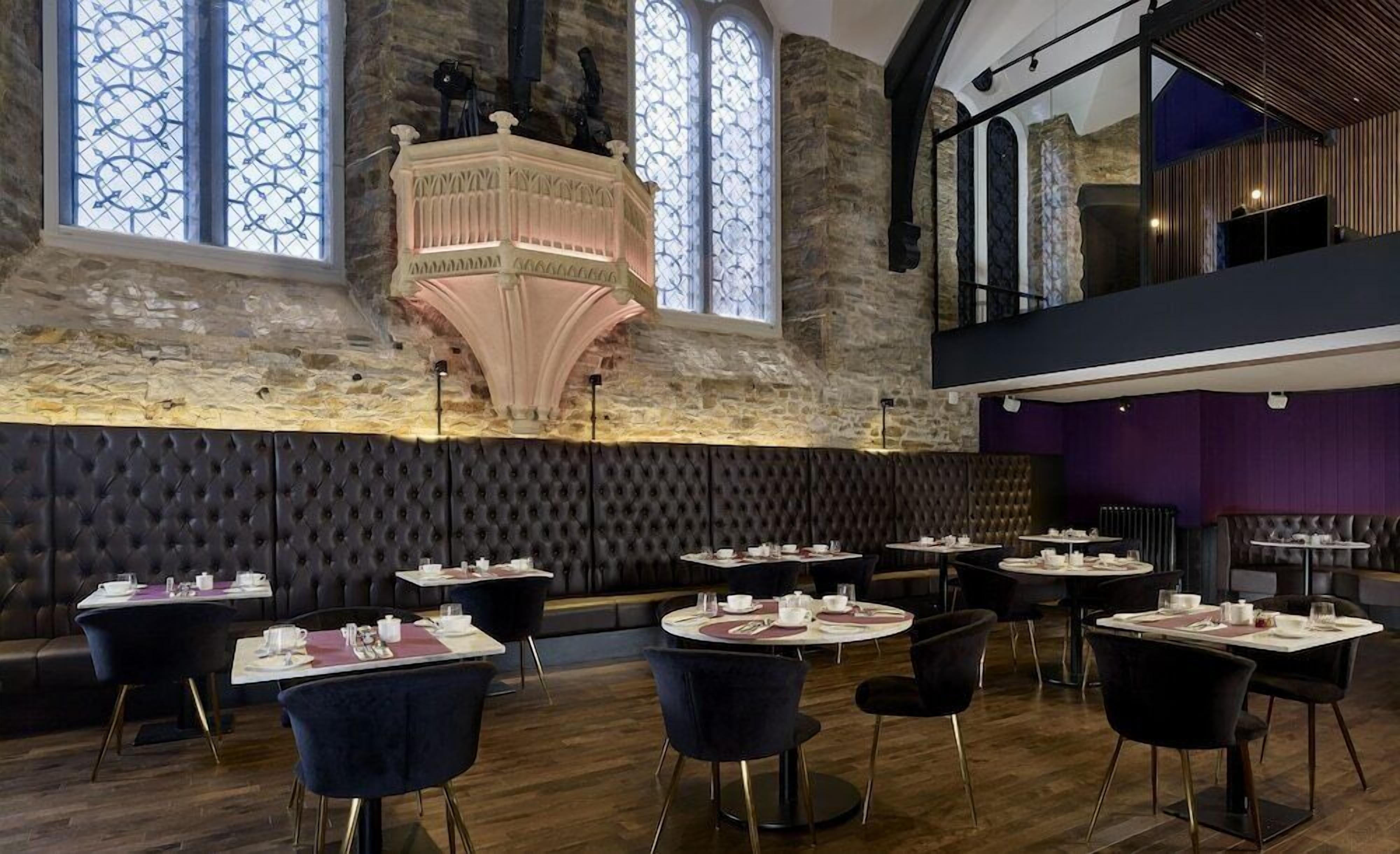 A restaurant with a stone wall, a decorative ceiling, and a view of the sky through large windows.