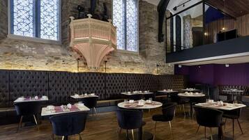 A restaurant with a stone wall, a decorative ceiling, and a view of the sky through large windows.