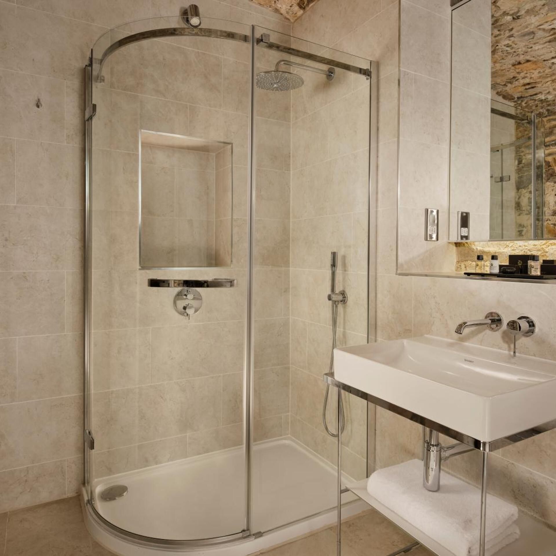 Een moderne badkamer met een glazen douchecabine, een wit wastafelmeubel en een stenen wand.