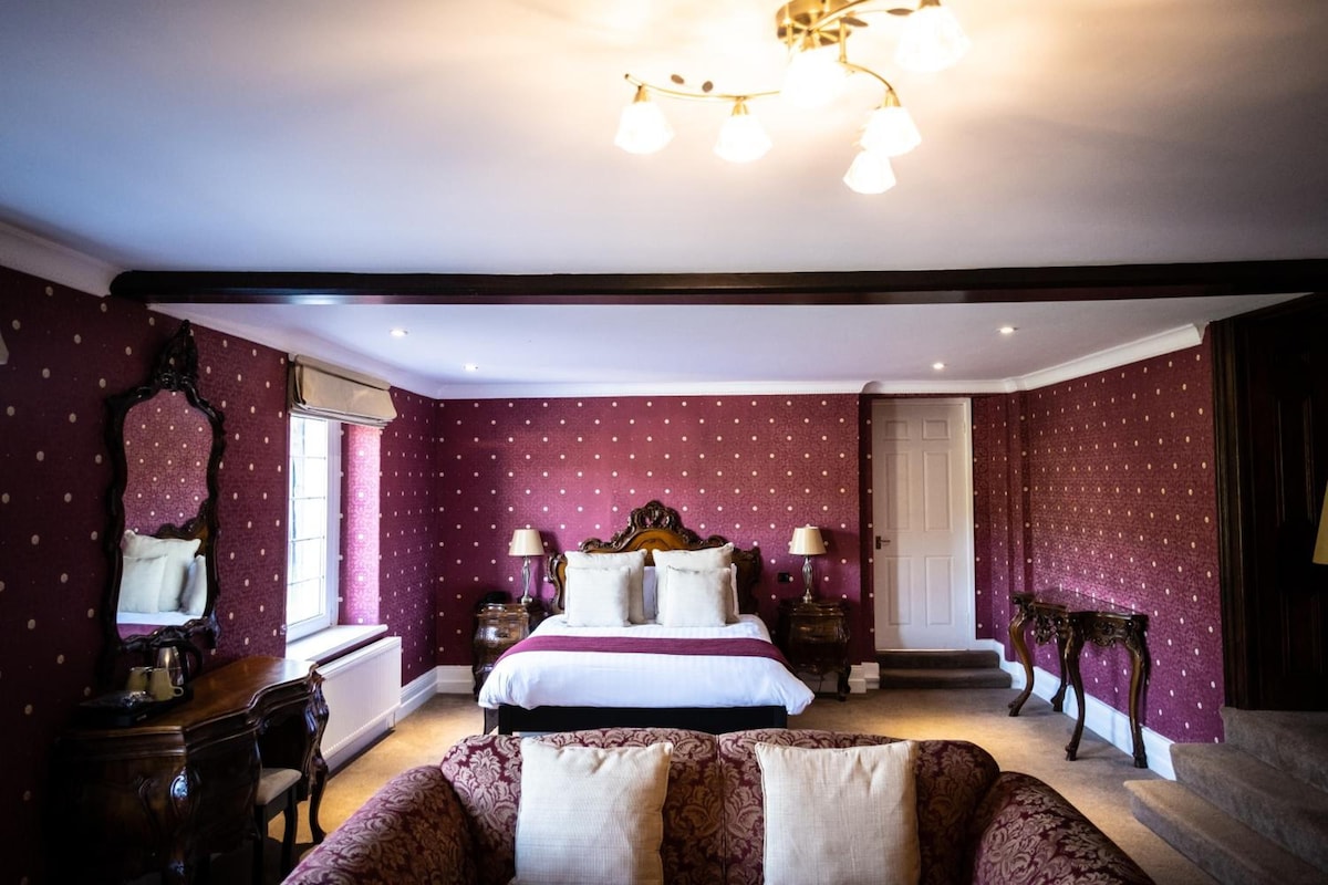 A bedroom with a bed, two bedside tables, a mirror, a chandelier, and a door.