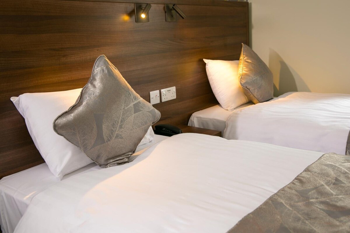 Two twin beds with white linens and decorative pillows, a wooden headboard, and a bedside table with a phone.