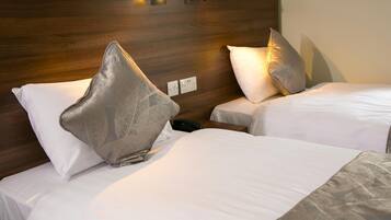 Two twin beds with white linens and decorative pillows, a wooden headboard, and a bedside table with a phone.