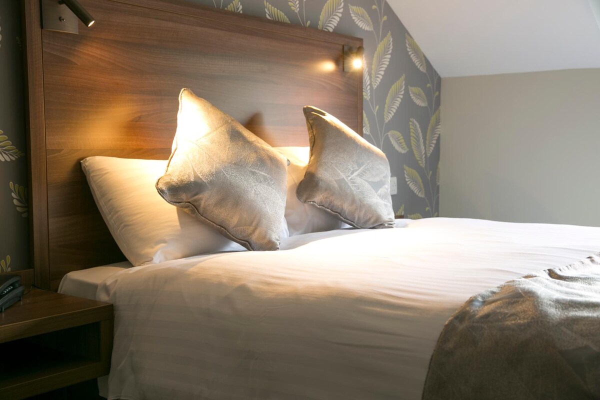 A hotel room with a wooden headboard, two pillows, a white bedspread, and a nightstand with a telephone.