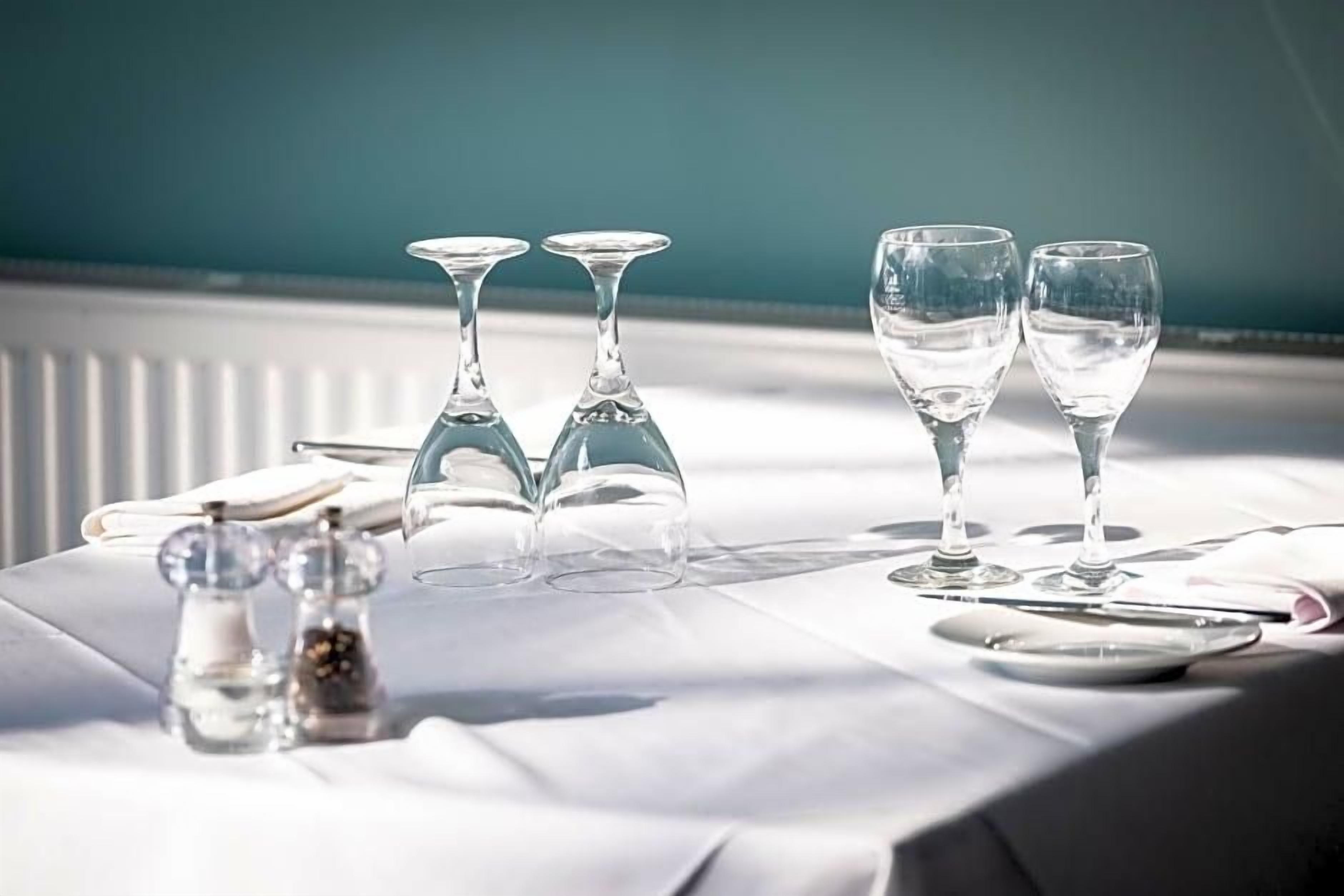 A table set with clear glasses, salt and pepper shakers, and a white tablecloth.