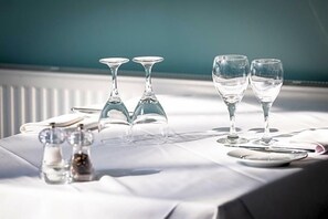 Taula posta amb vasos de cristall, salabros i pebreros, i un mantell de taula blanc.
